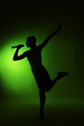 Photo of Silhouette of woman singing on dark background with green light