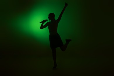 Photo of Silhouette of woman singing on dark background with green light