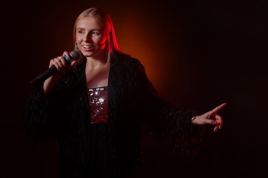 Photo of Beautiful singer performing on dark background with orange light. Space for text