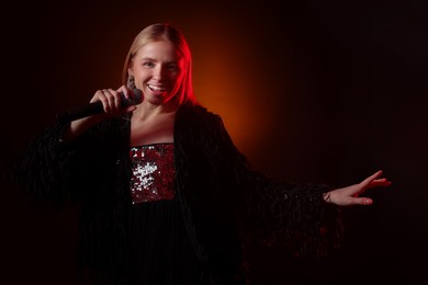 Photo of Beautiful singer performing on dark background with orange light. Space for text