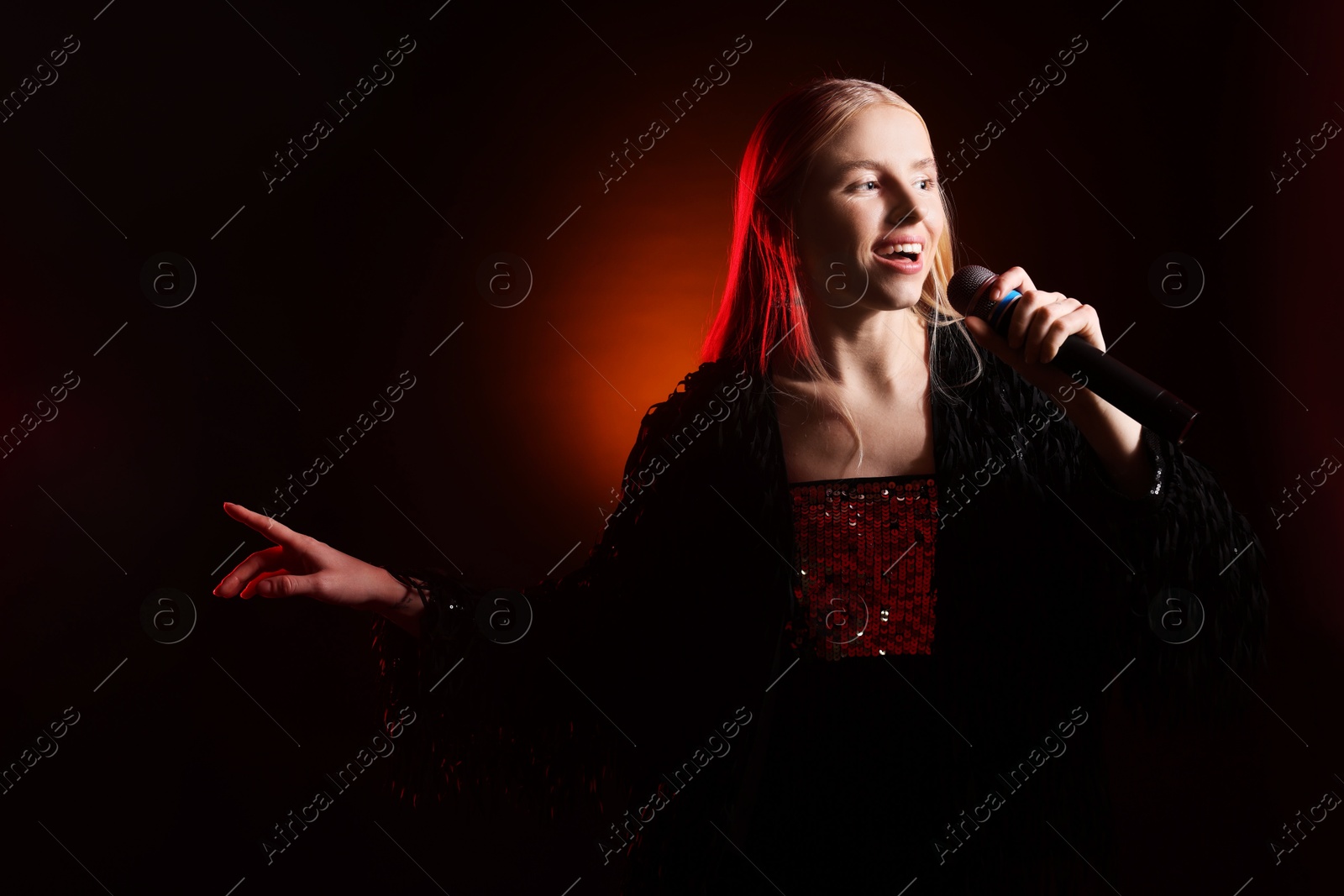 Photo of Beautiful singer performing on dark background with orange light. Space for text