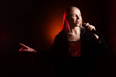 Beautiful singer performing on dark background with orange light. Space for text