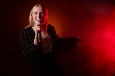 Beautiful singer performing on dark background with red light and smoke. Space for text