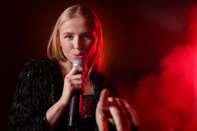 Photo of Beautiful singer performing on dark background with red light and smoke. Space for text