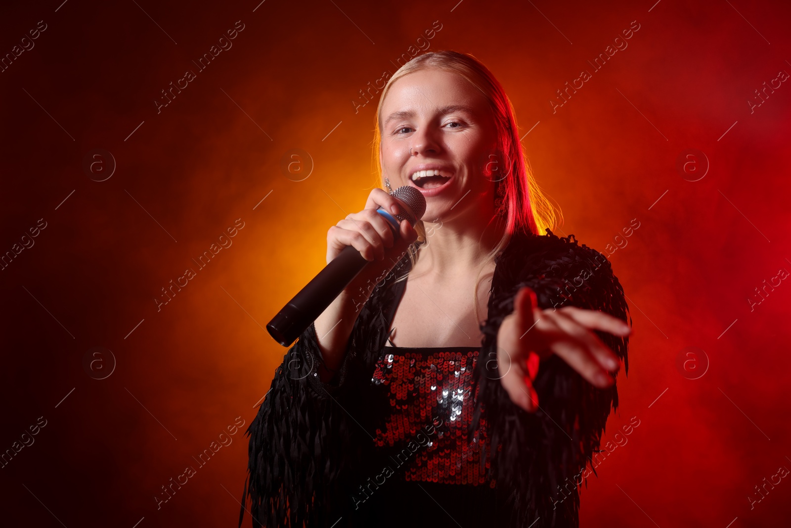 Photo of Beautiful singer performing on dark background with orange light and smoke