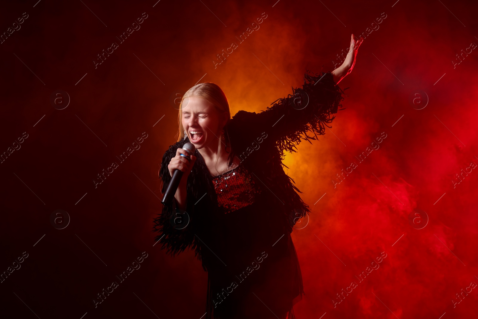 Photo of Beautiful singer performing on dark background with red light and smoke