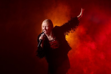 Photo of Beautiful singer performing on dark background with red light and smoke