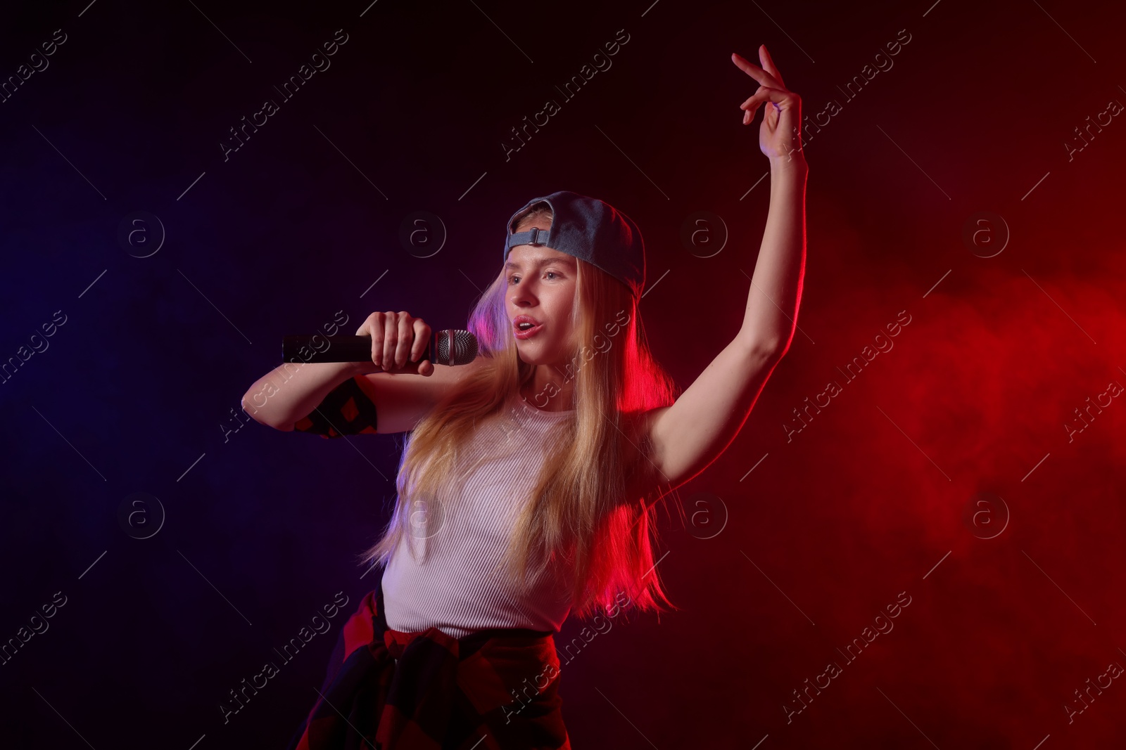 Photo of Talented singer performing on dark background with color lights and smoke