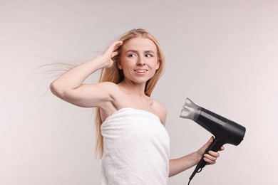 Photo of Beautiful young woman drying her hair with hairdryer on light grey background