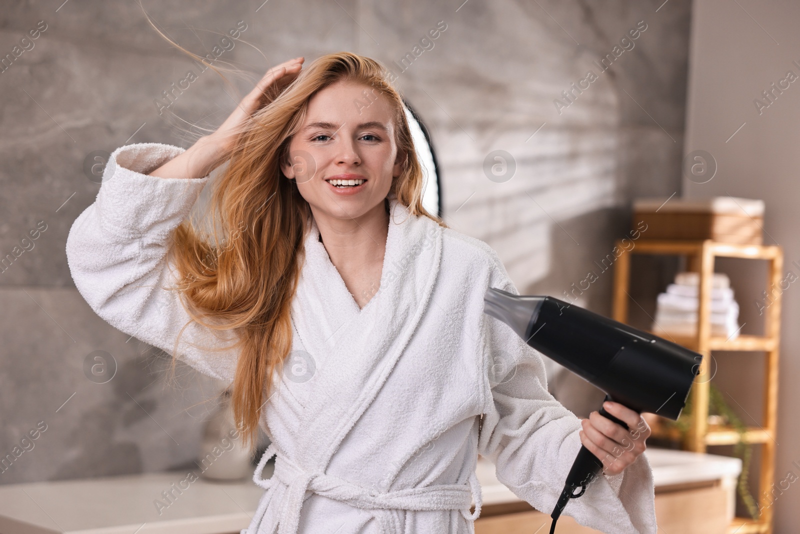 Photo of Beautiful young woman drying her hair in bathroom