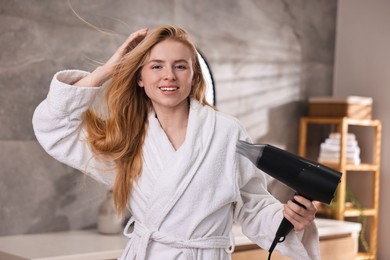 Photo of Beautiful young woman drying her hair in bathroom