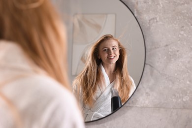 Photo of Beautiful young woman drying her hair near mirror in bathroom