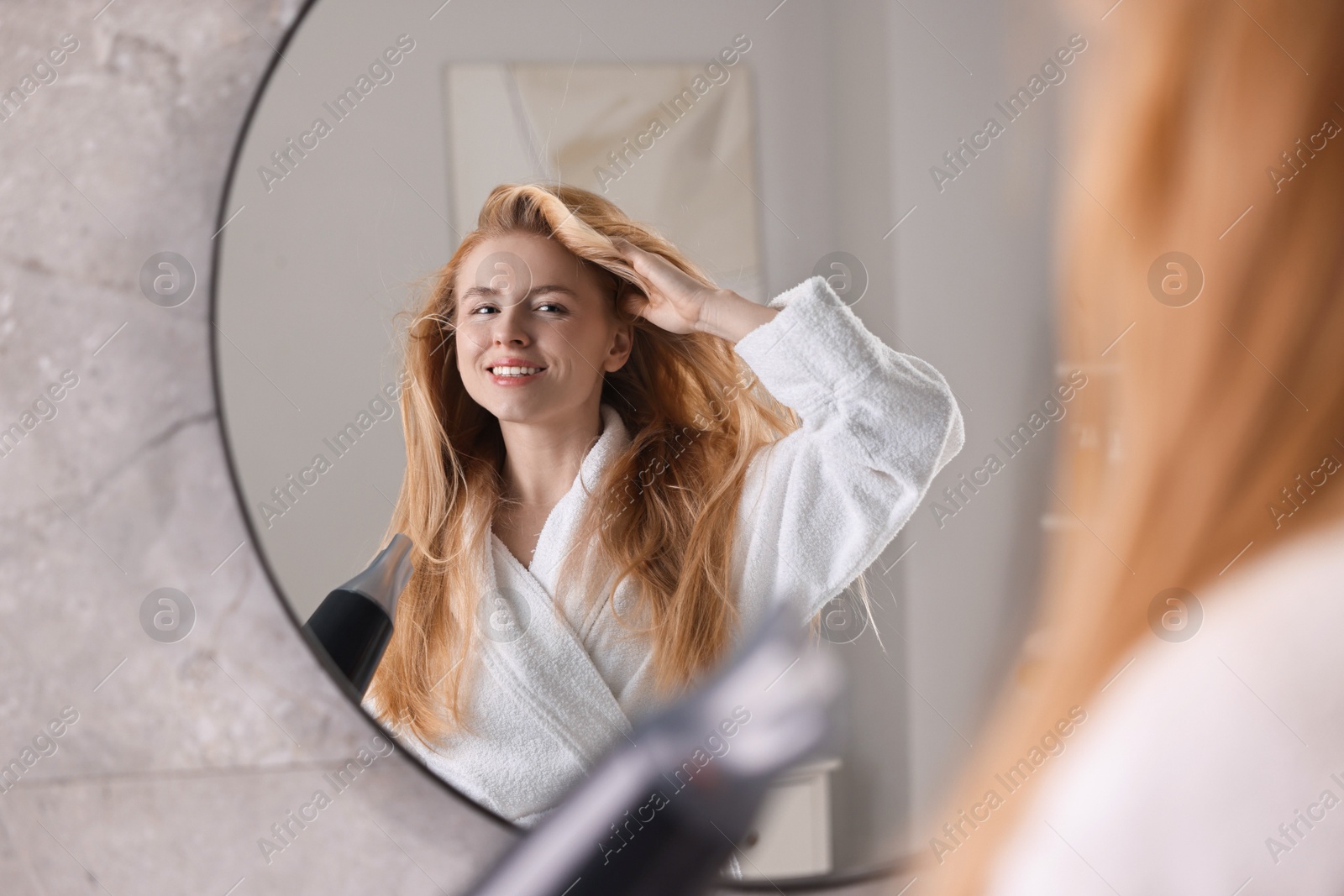 Photo of Beautiful young woman drying her hair near mirror in bathroom