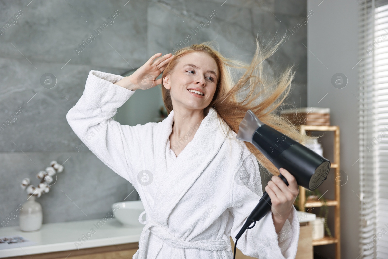 Photo of Beautiful young woman drying her hair in bathroom