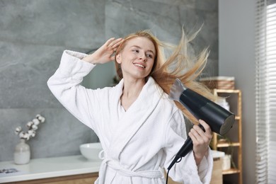 Beautiful young woman drying her hair in bathroom