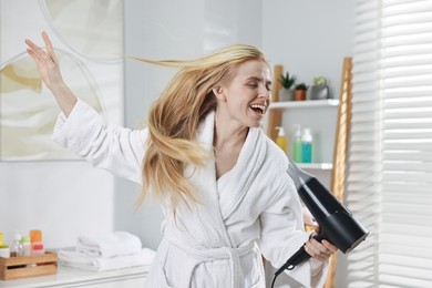 Photo of Beautiful young woman drying her hair and singing in bathroom