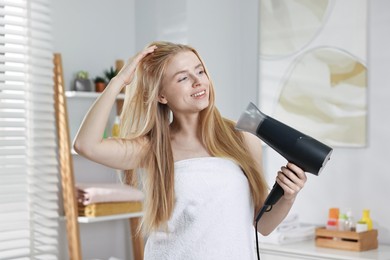 Photo of Beautiful young woman drying her hair in bathroom