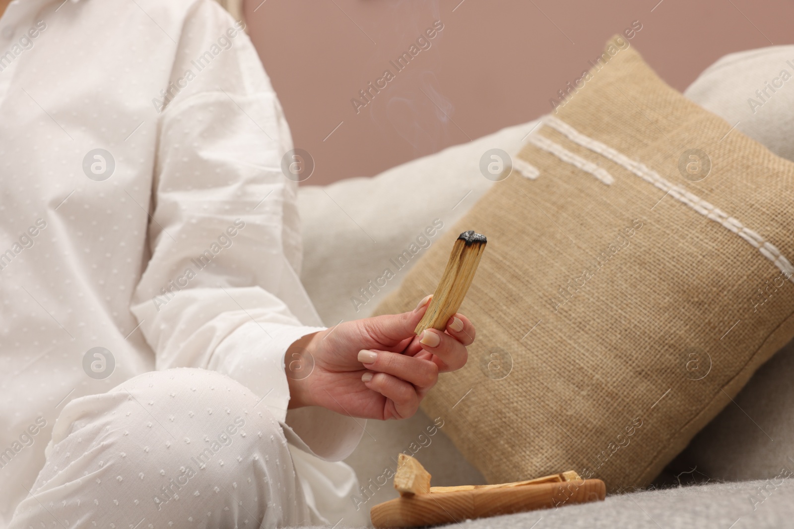 Photo of Woman with smoldering palo santo stick meditating on sofa at home, closeup