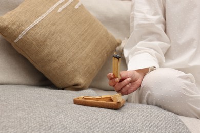 Photo of Woman with burning palo santo stick meditating on sofa at home, closeup. Space for text