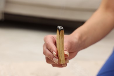 Photo of Woman with smoldering palo santo stick at home, closeup