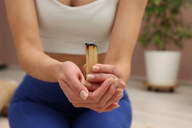 Photo of Woman with smoldering palo santo stick at home, closeup