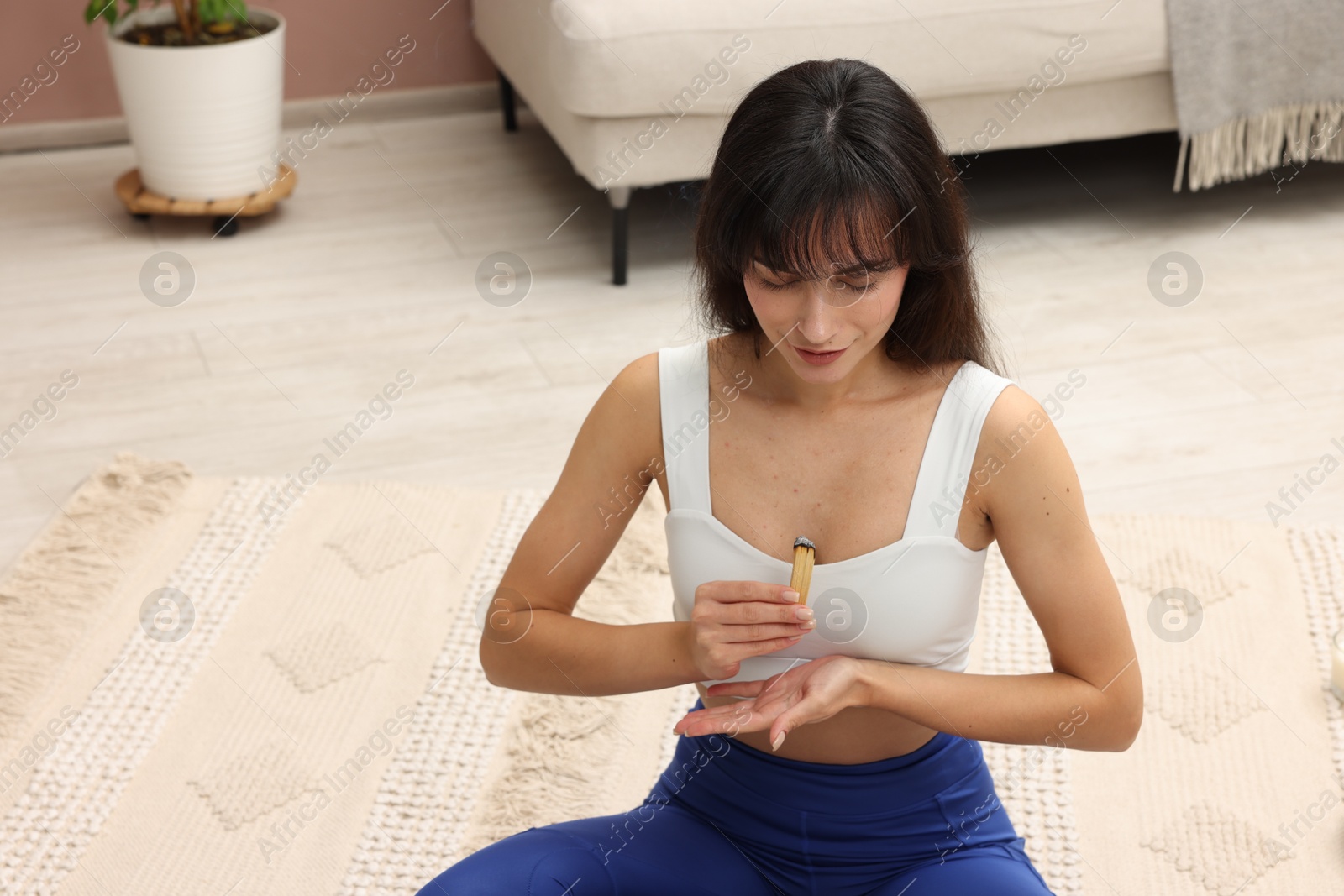 Photo of Woman with smoldering palo santo stick on floor at home, space for text