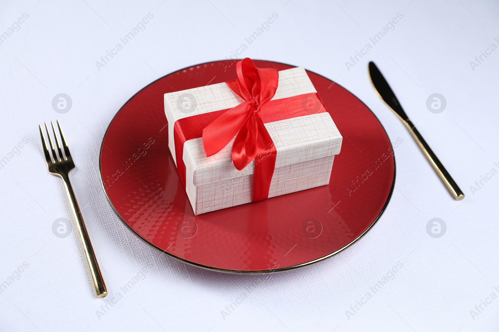 Photo of Gift box, plate and cutlery on white table, closeup. Beautiful table setting for romantic dinner