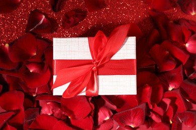 Beautiful gift box and rose petals on red glitter background, flat lay. Romantic present