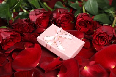 Photo of Beautiful gift box among rose flowers and petals, closeup. Romantic present