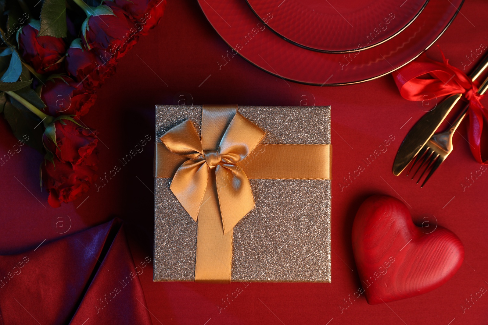 Photo of Gift box, roses and tableware on red table, flat lay. Table setting for romantic Valentine's day celebration