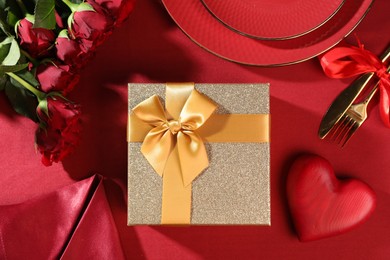 Photo of Gift box, roses and tableware on red table, flat lay. Table setting for romantic Valentine's day celebration