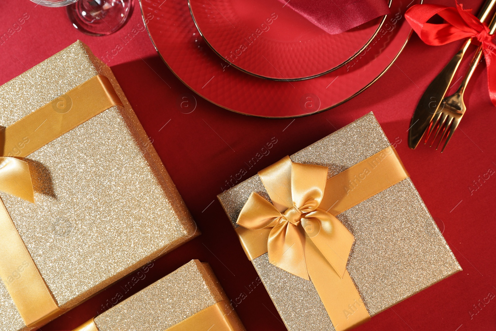 Photo of Gift boxes and tableware on red table, flat lay. Table setting for romantic dinner