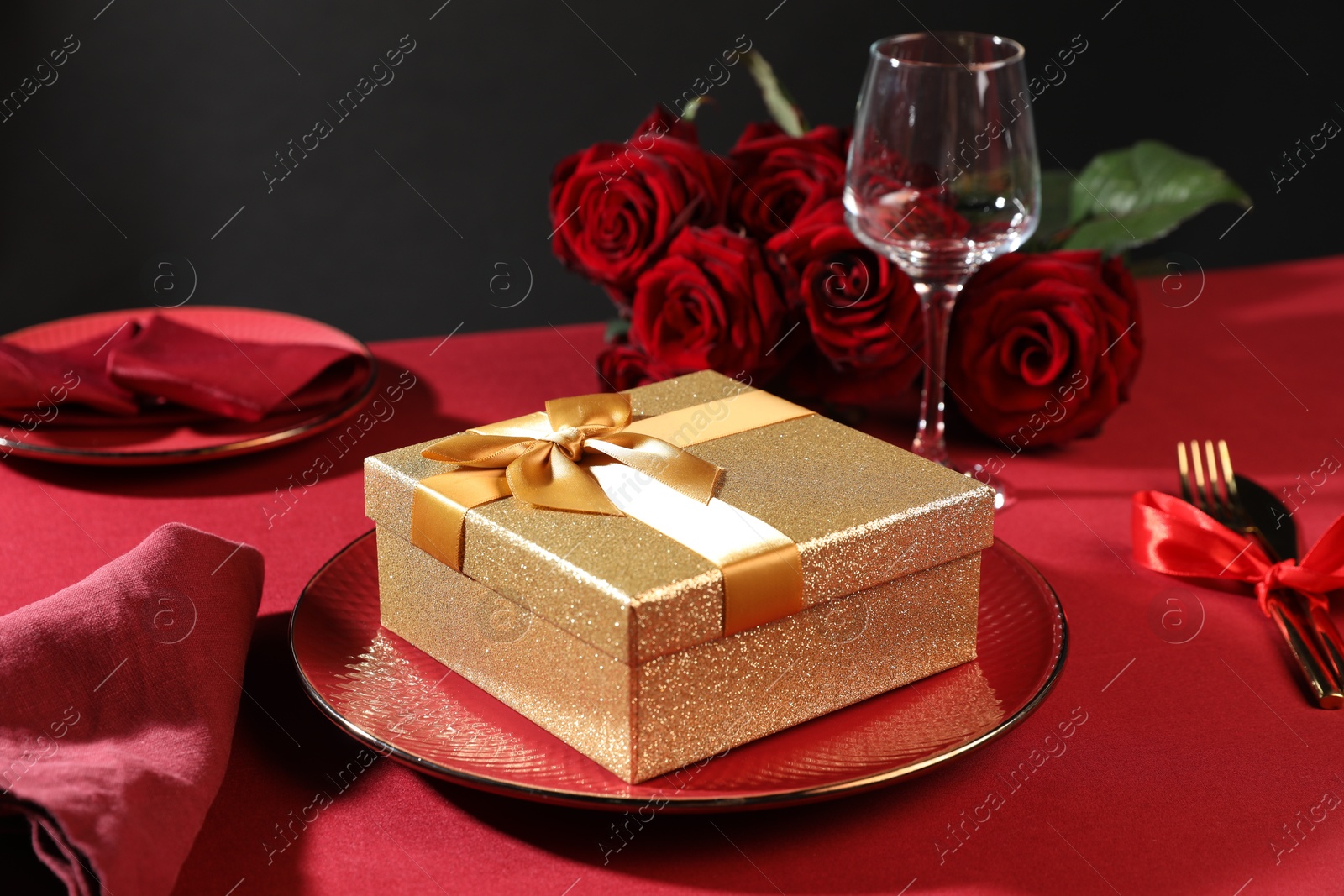 Photo of Gift box, plate and roses on red table, closeup. Table setting for romantic dinner