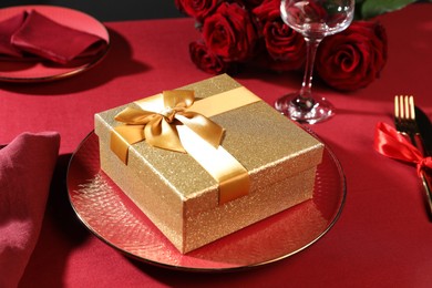 Gift box, plate and roses on red table, closeup. Table setting for romantic dinner