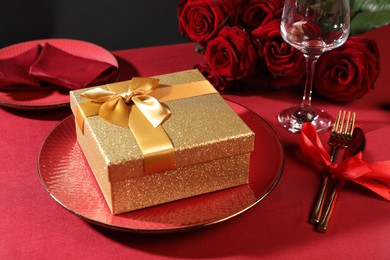 Photo of Gift box, plate and roses on red table, closeup. Table setting for romantic dinner