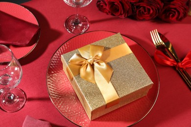 Photo of Gift box and tableware on red table. Table setting for romantic dinner