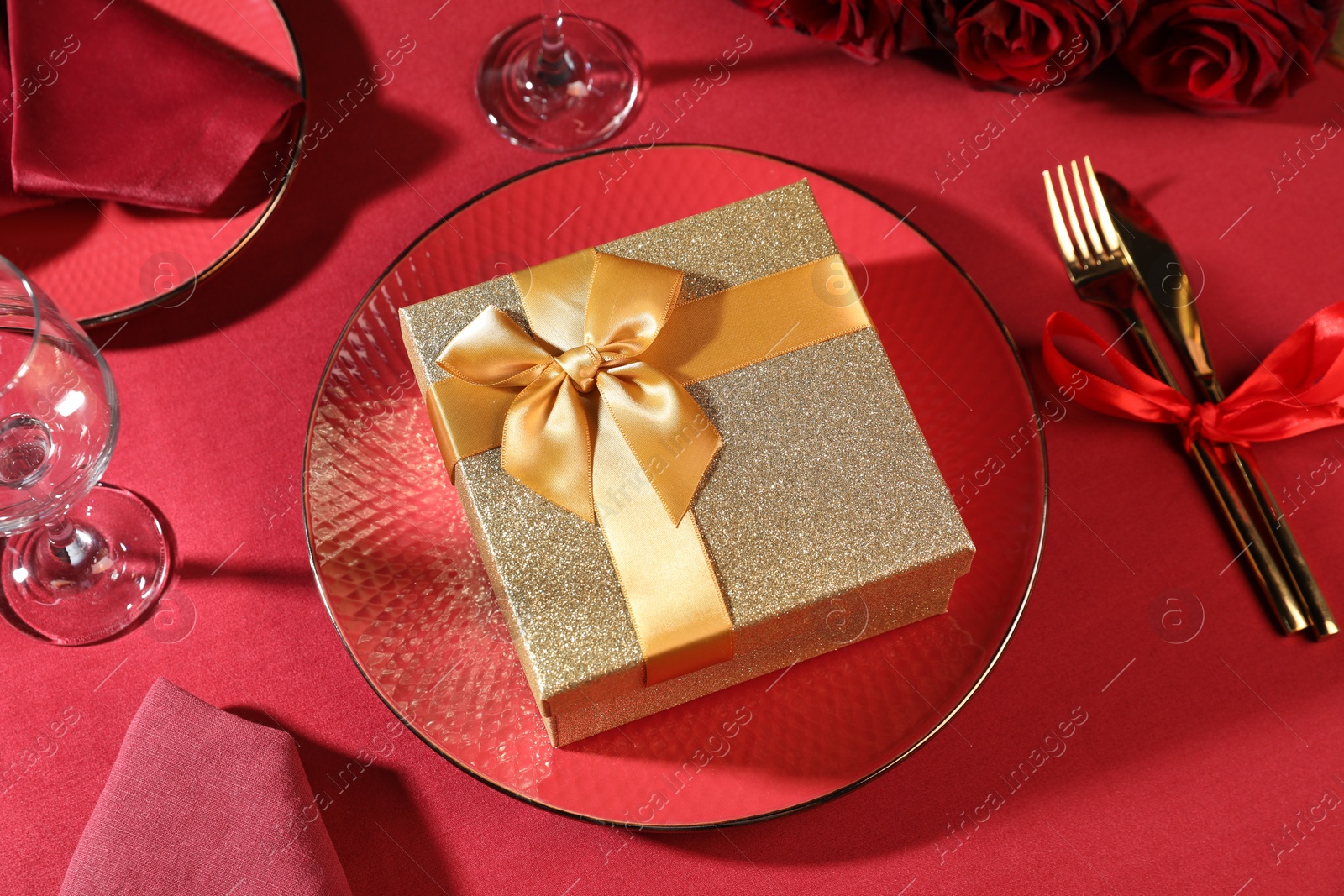 Photo of Gift box and tableware on red table. Table setting for romantic dinner