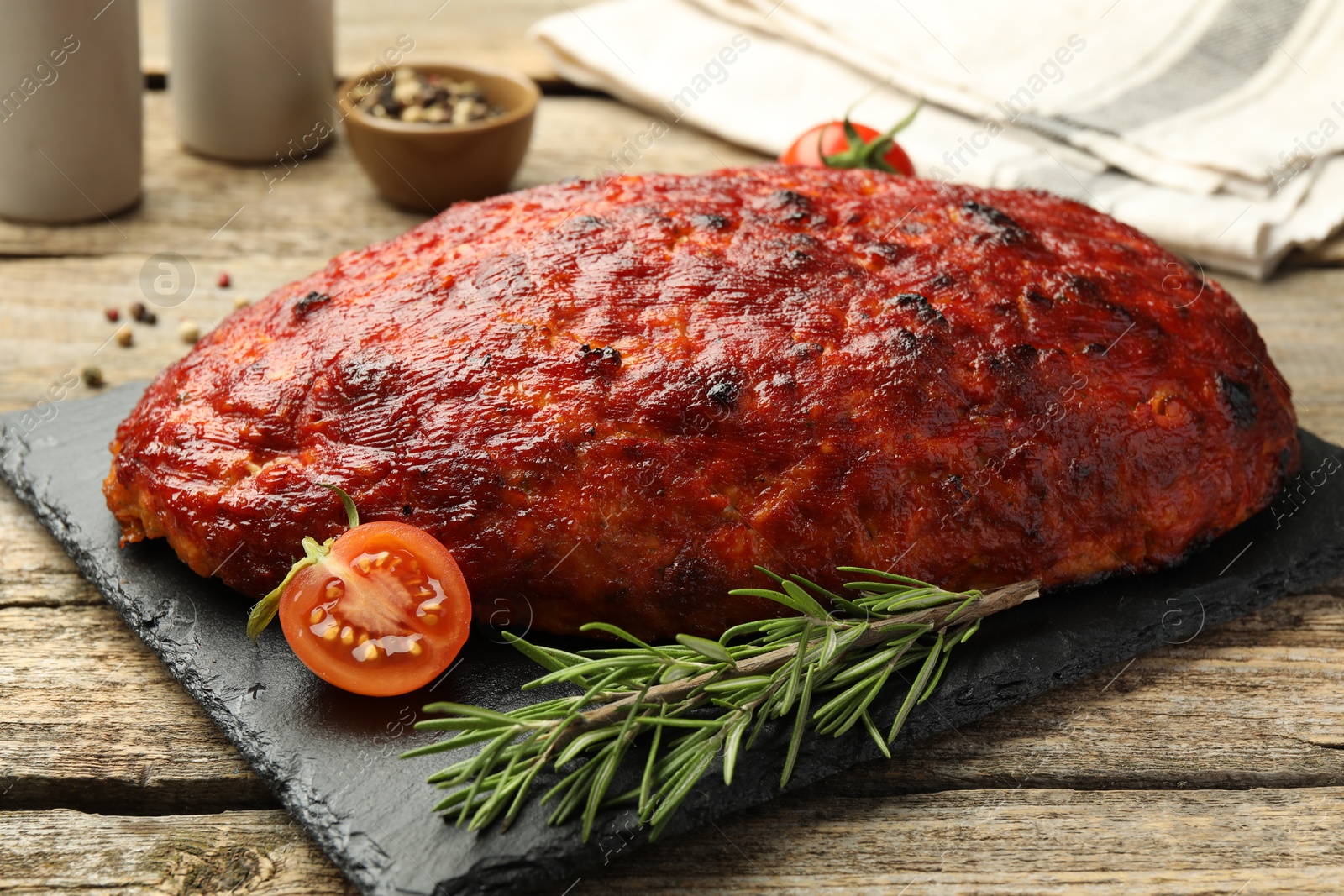 Photo of Delicious turkey meatloaf with tomatoes and rosemary on wooden table, closeup