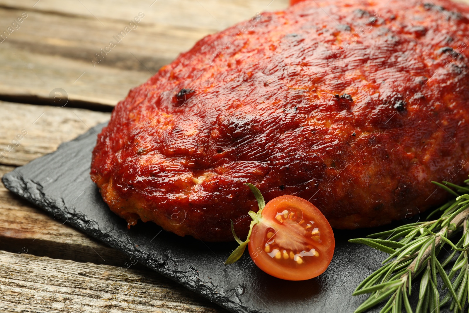 Photo of Delicious turkey meatloaf with tomato and rosemary on wooden table, closeup