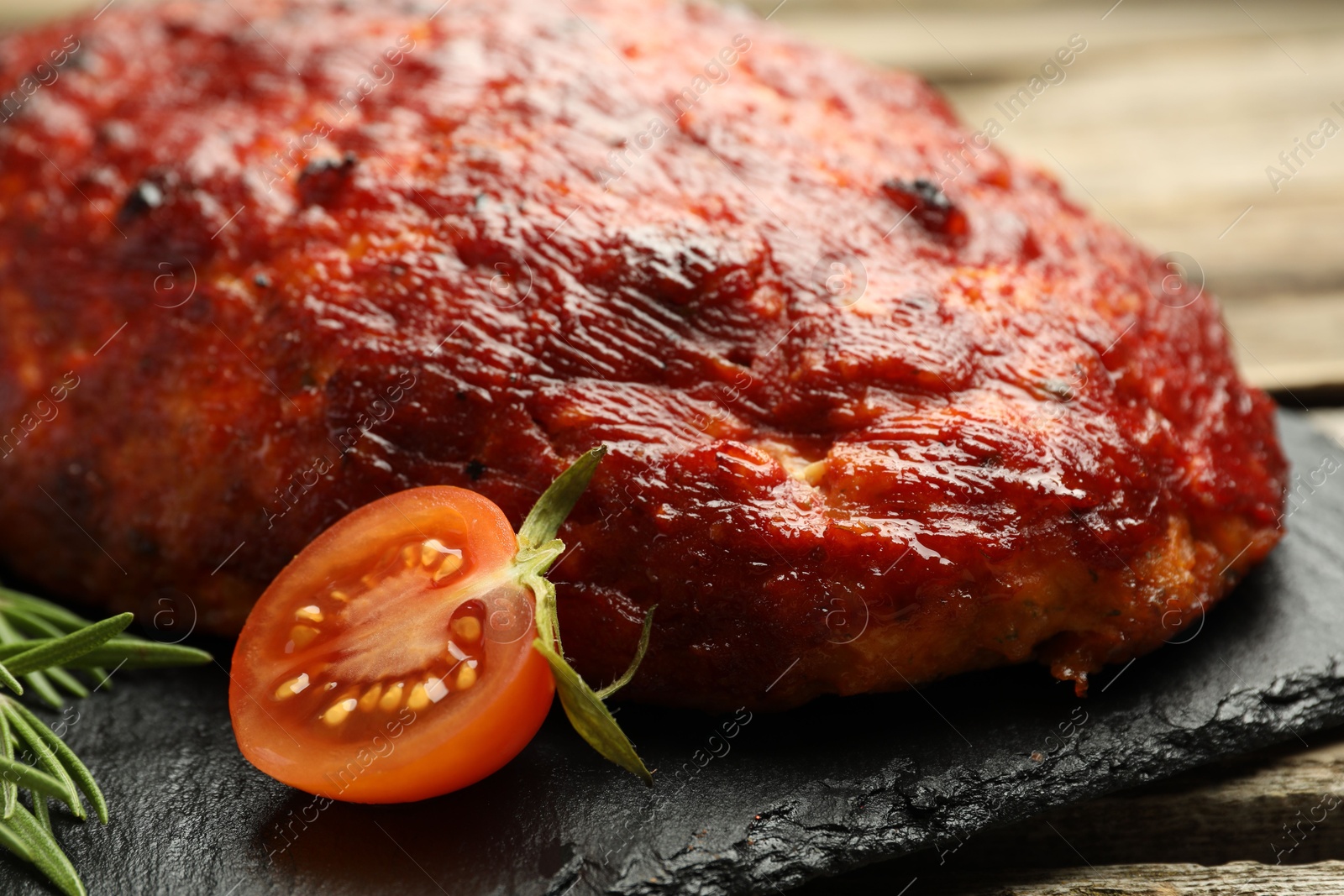 Photo of Delicious turkey meatloaf with tomato and rosemary on wooden table, closeup