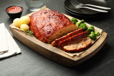 Photo of Delicious turkey meatloaf with vegetables served on black table, closeup