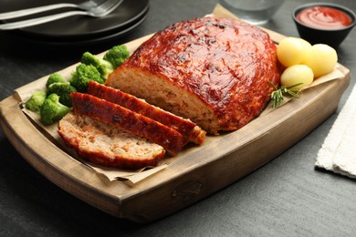 Photo of Delicious turkey meatloaf with vegetables served on black table, closeup