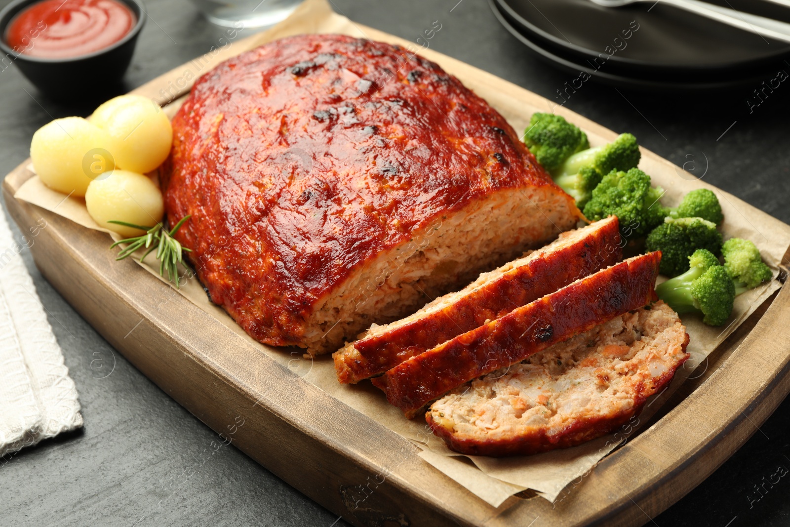 Photo of Delicious turkey meatloaf with vegetables served on black table, closeup