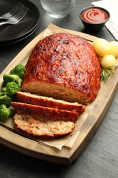 Photo of Delicious turkey meatloaf with vegetables served on black table, closeup