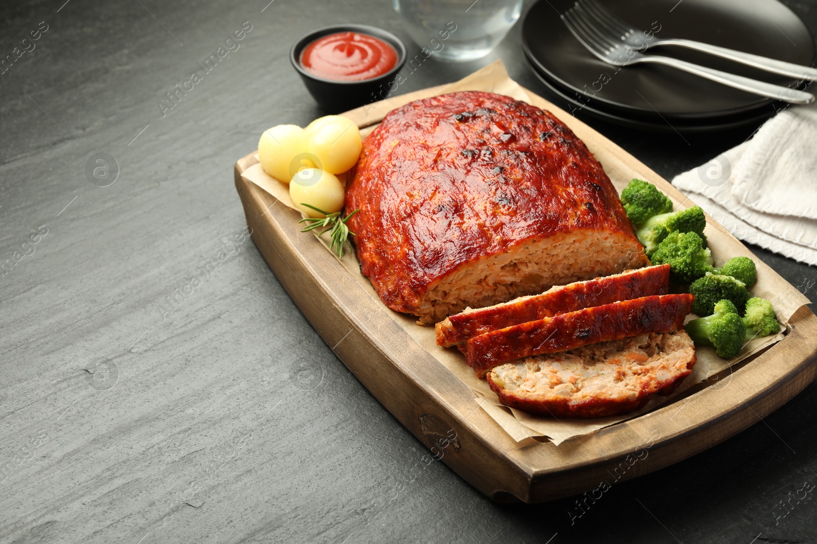 Photo of Delicious turkey meatloaf with vegetables served on black table, closeup. Space for text