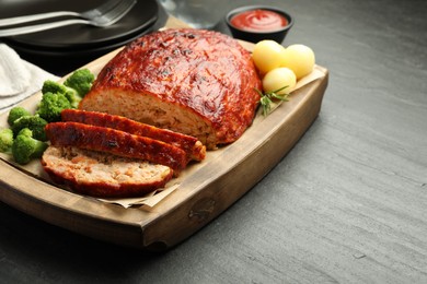 Photo of Delicious turkey meatloaf with vegetables served on black table, closeup