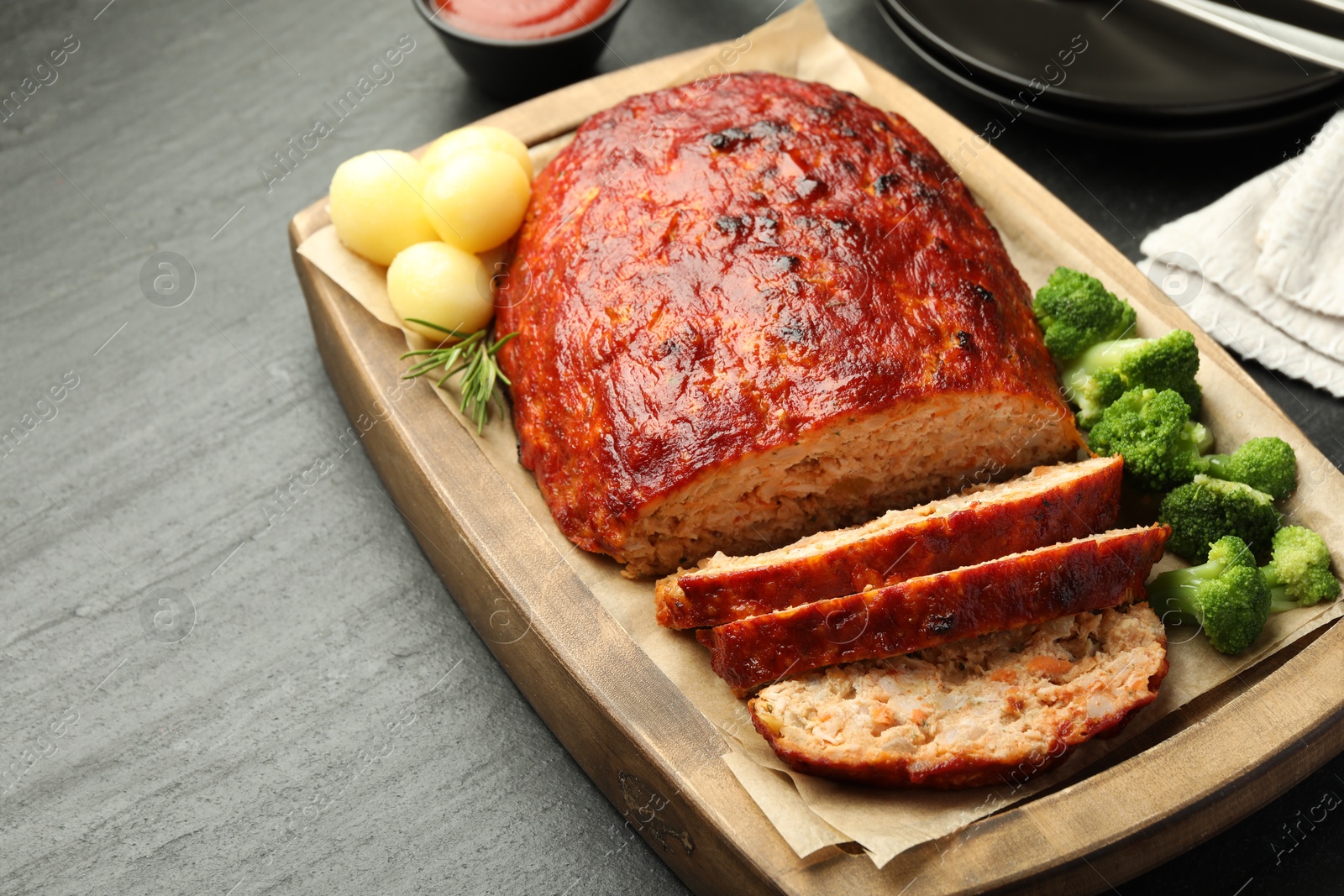 Photo of Delicious turkey meatloaf with vegetables served on black table, closeup