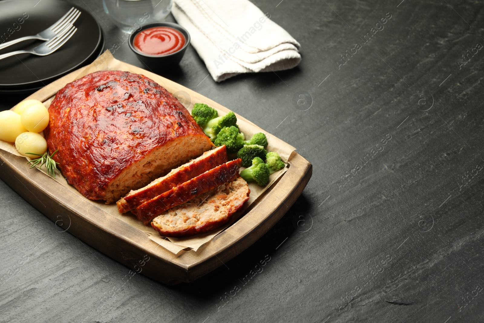 Photo of Delicious turkey meatloaf with vegetables served on black table. Space for text