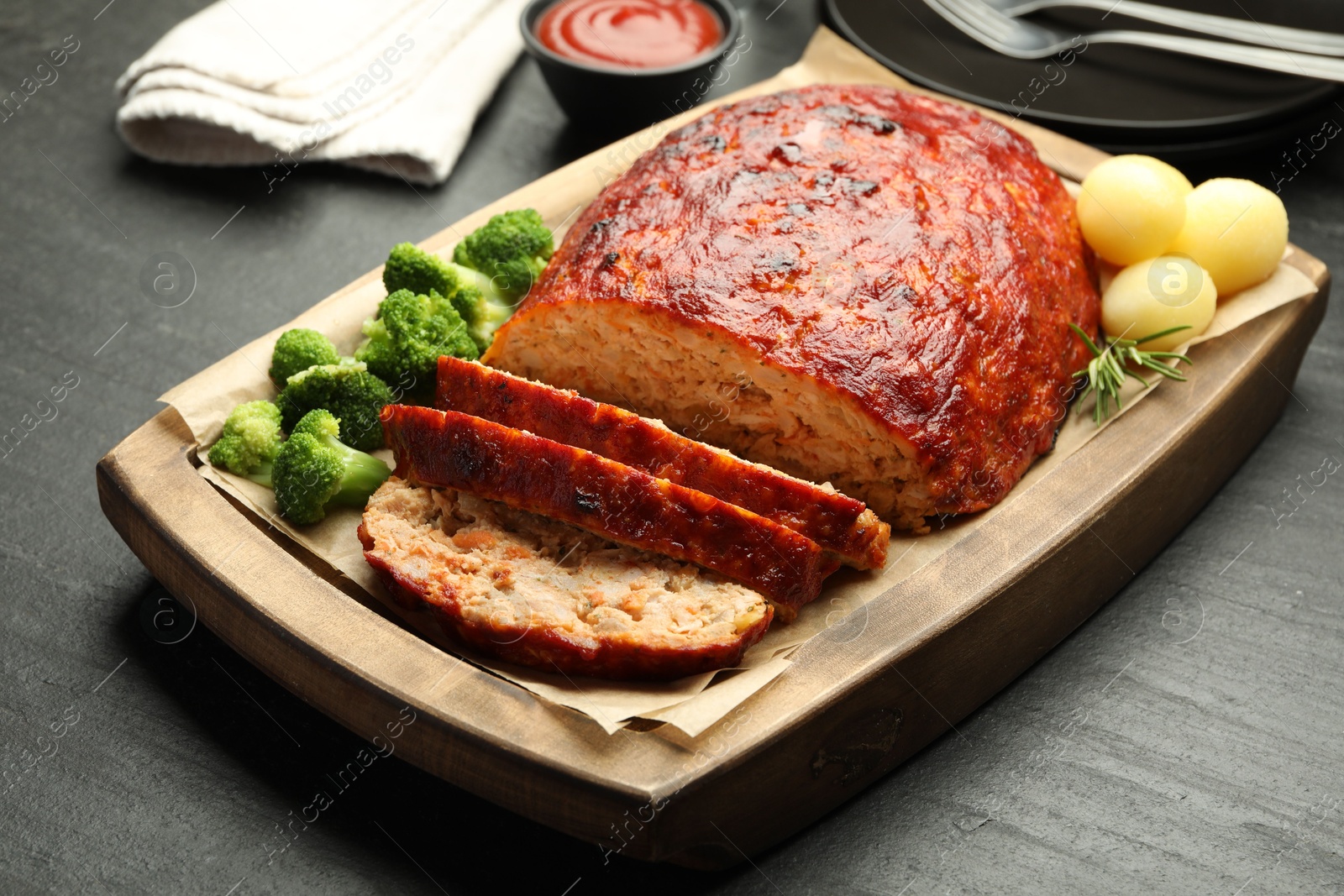 Photo of Delicious turkey meatloaf with vegetables served on black table, closeup