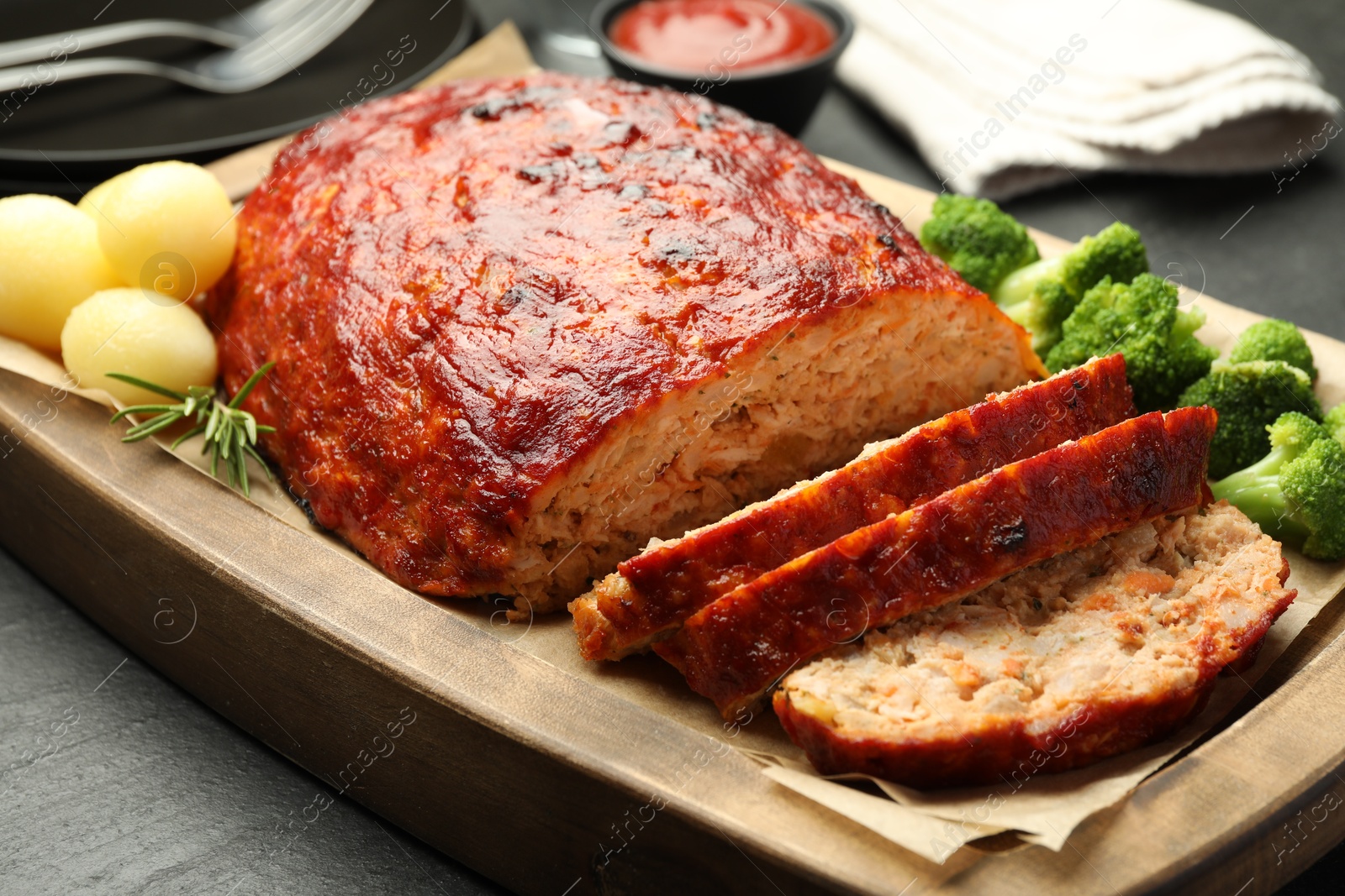 Photo of Delicious turkey meatloaf with vegetables served on black table, closeup